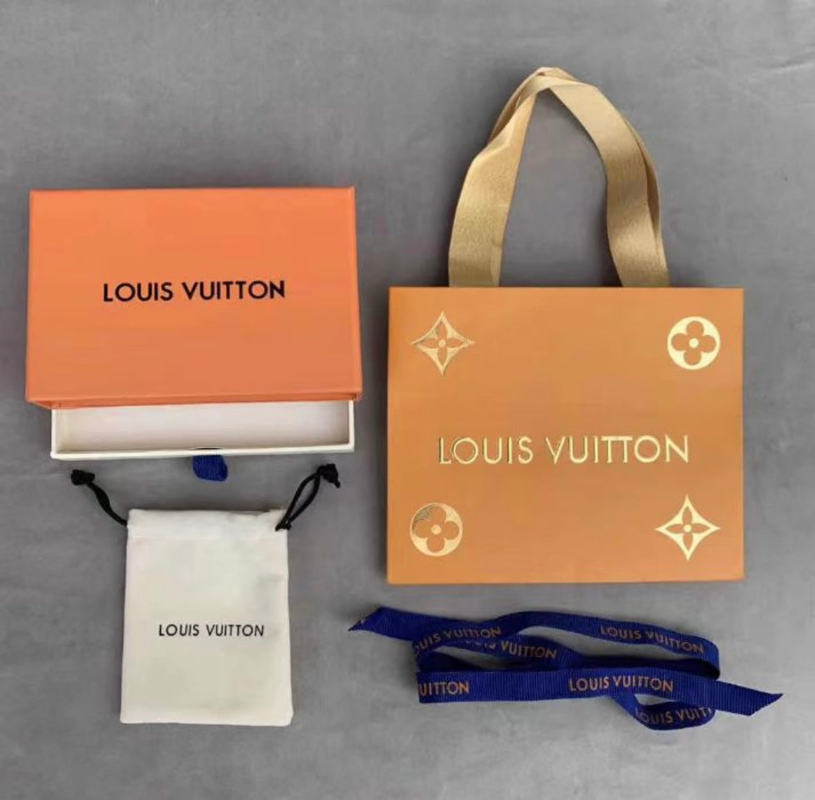 Louis Vuitton packaging including box, pouch, and ribbons on a gray background