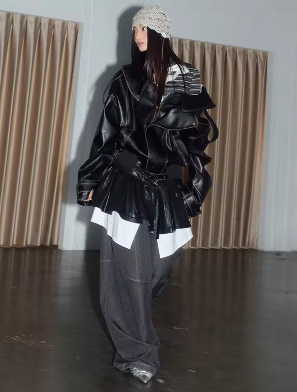 Person wearing a black layered outfit with a white patterned top against a plain background