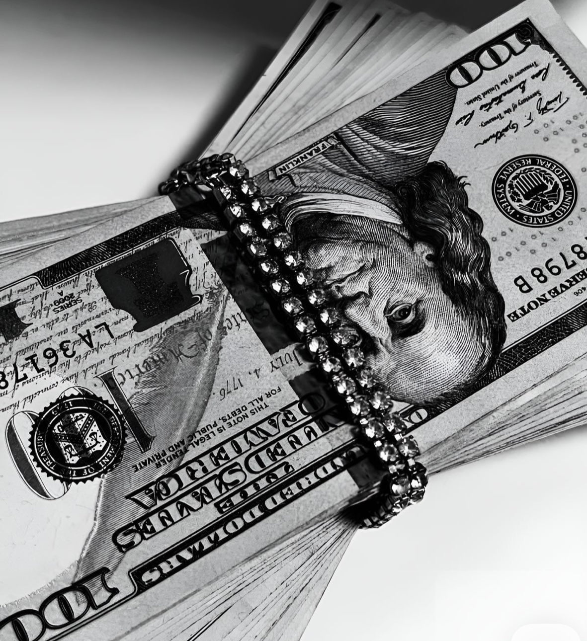 A close-up black-and-white photo of a stack of $100 bills wrapped with a rhinestone-covered money band.