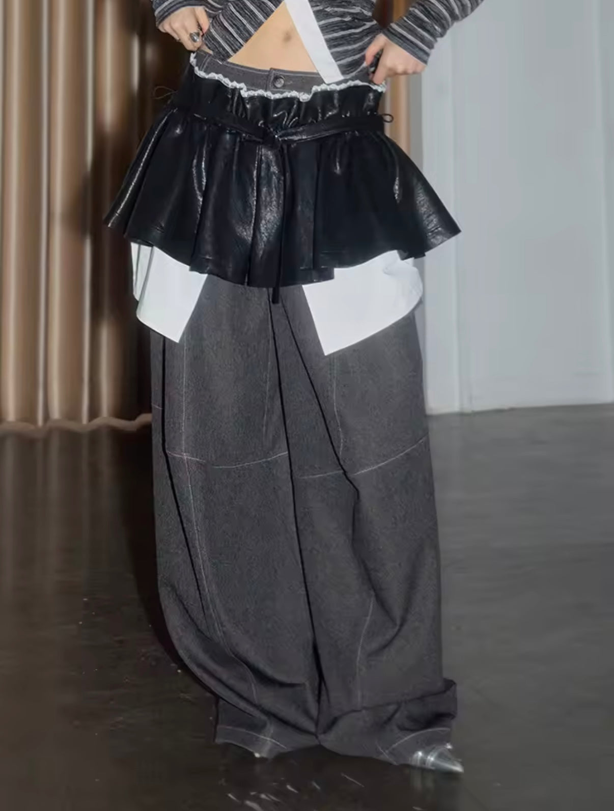 Person wearing a black leather skirt over a white shirt with gray wide-leg pants.