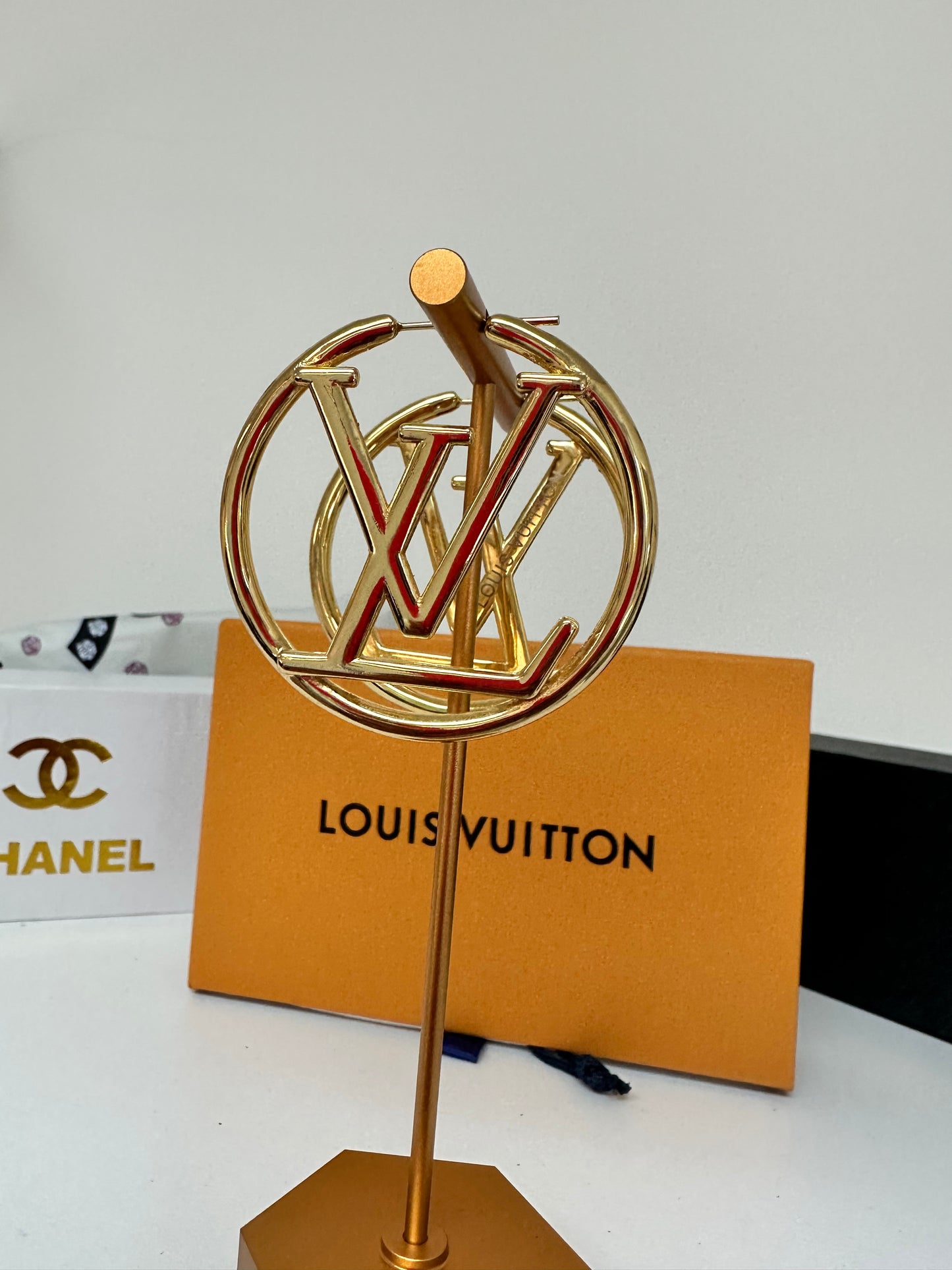 Gold earring on a white surface with a Louis Vuitton box in the background