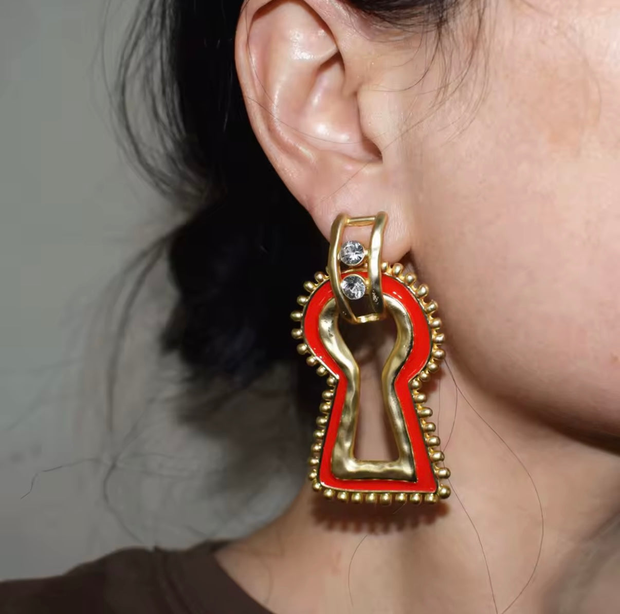 Gold and red earring worn by a person with a neutral background