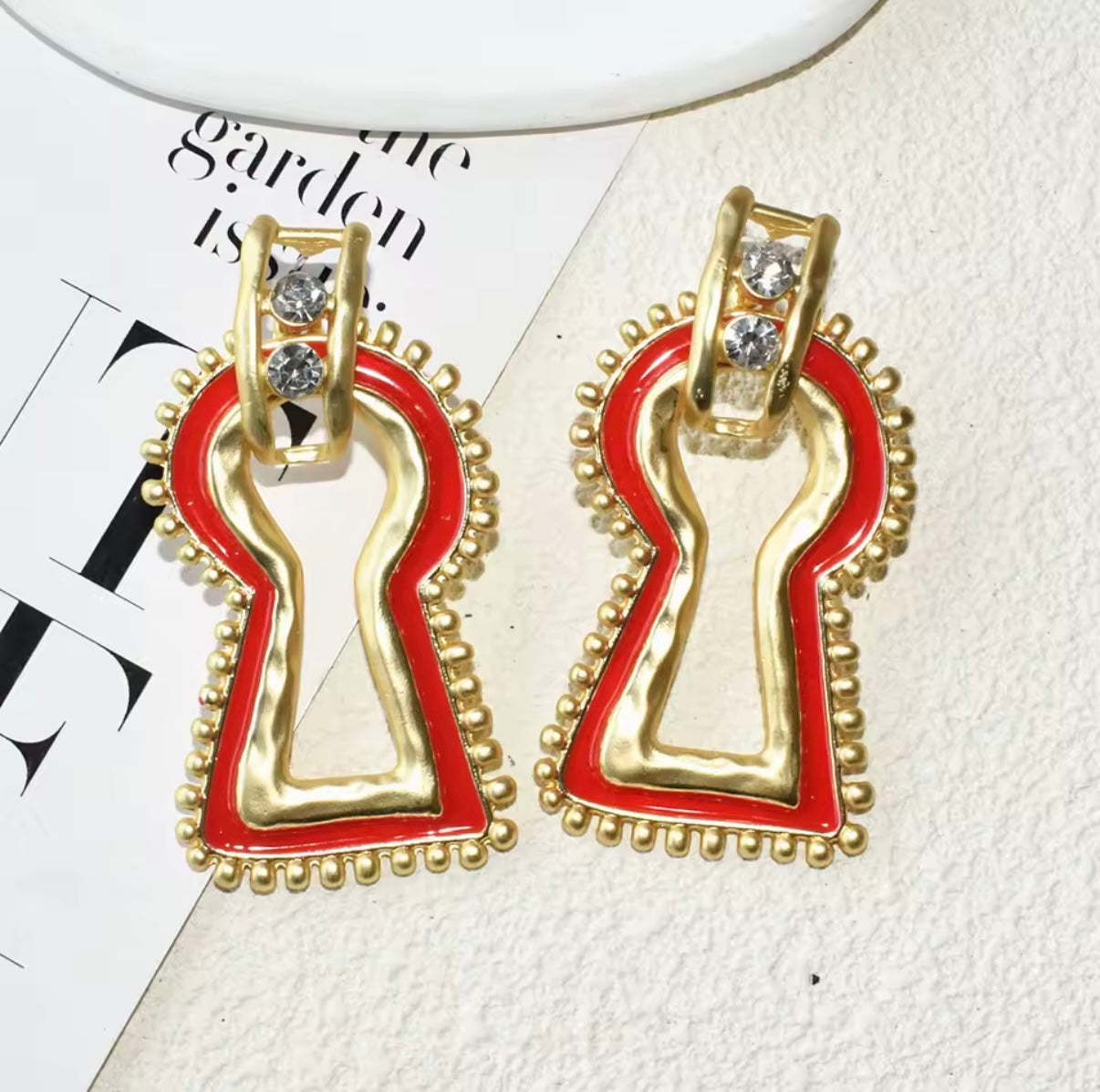 Gold and red keyhole-shaped earrings on a magazine page